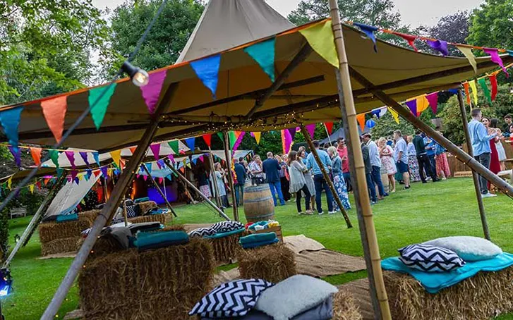 Tipis decorate with colourful flags, with partygoers enjoying a party in a garden