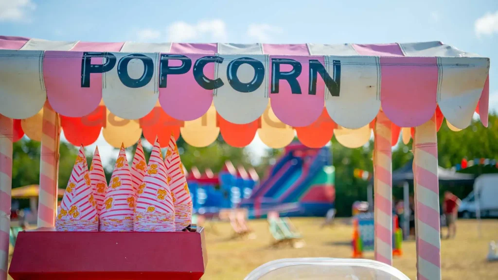 A close up image of a popcorn machine with festiva games and tents in the background. corporate event ideas