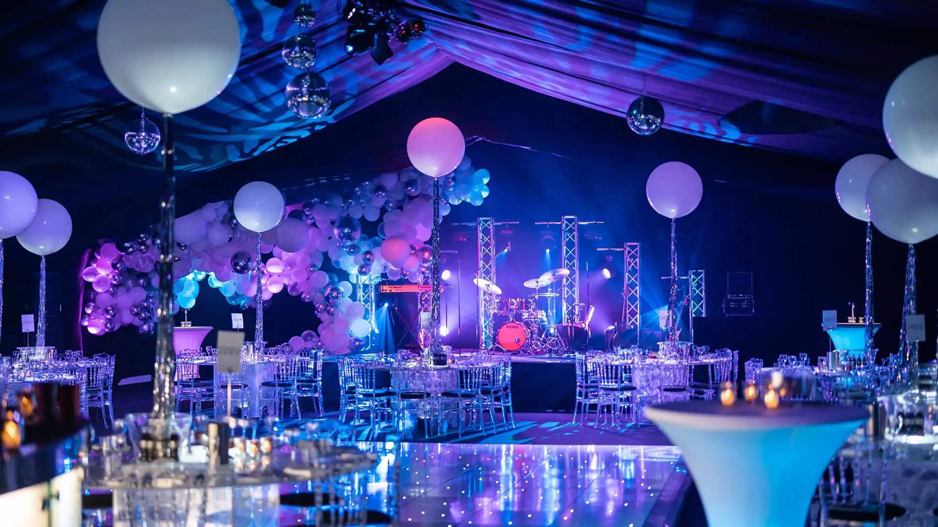 A stage in a marquee featuring full band equipment, with a dancefloor in front, lighting and lots of balloons for used to decorate the marquee