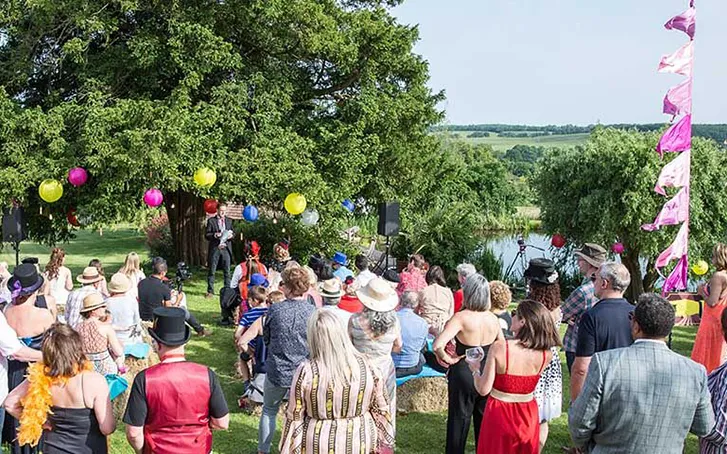 A crowd gathered to watch a circus performer at an outdoor corporate event in summer. Trees in the background and a blue sky overhead.