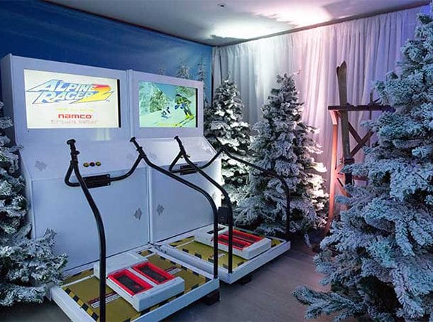 A Christmas-themed arcade room with snow-covered trees. Two arcade games called Alpine Racer for a skiing game.