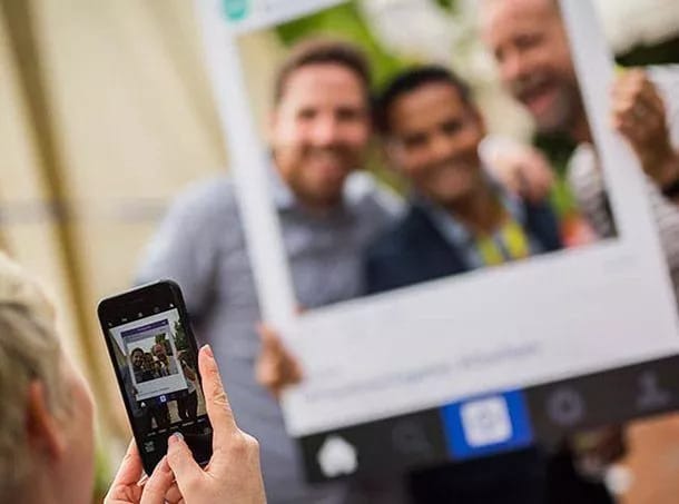 An image of a person taking a photo of three other people inside a physical frame. The people in frame are out of focus.