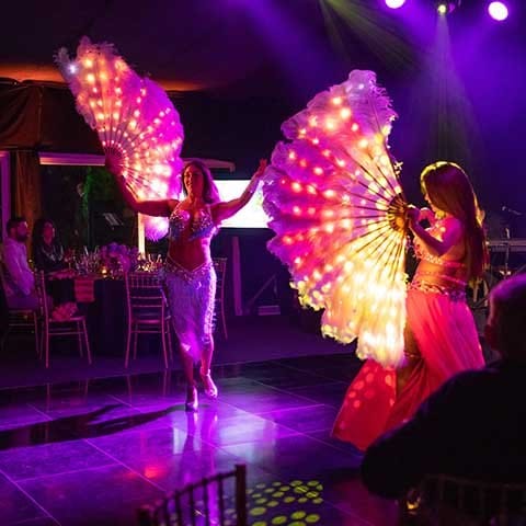 An image of a party with two women holding giant feathered fans as entertainment for the people sitting at the sides.