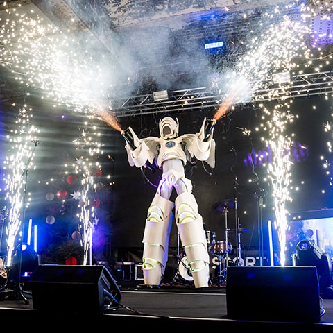 A large robot on the stage. The robot is shooting sparks from the robot ‘hands’, creating a firework-like effect.